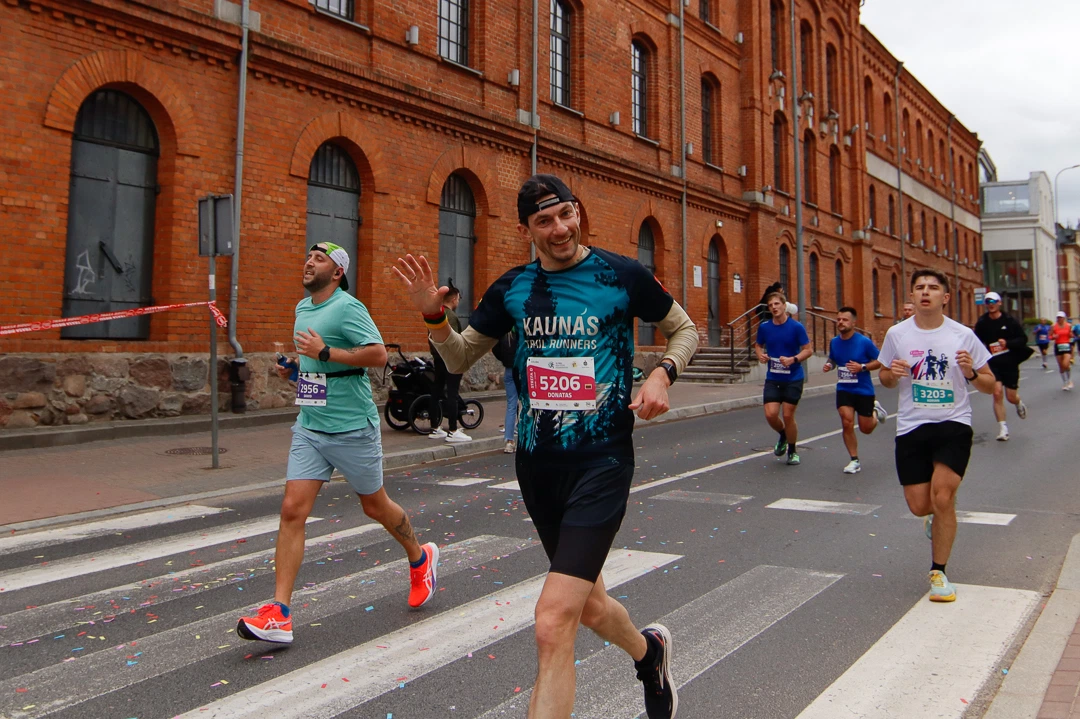 Uśmiechnięty zawodnik pozdrawiający fotografa na tle długiego ceglanego budynku