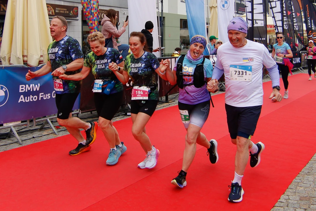 Grupa uśmiechniętych uczestników półmaratonu wspólnie przekraczających linię mety